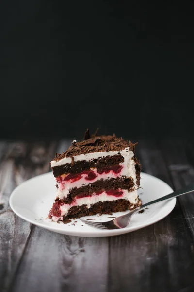 白い皿の上の暗い木製のテーブル背景にナプキン添えチョコレート ケーキ作品はさくらんぼとヨーグルト充填 — ストック写真