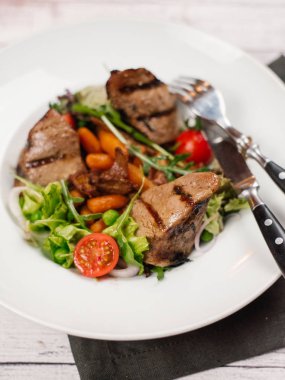 Izgara fileto mignon parçaları bebek havuç, domates, marul ve beyaz tabakta roka ile görünümünü portre