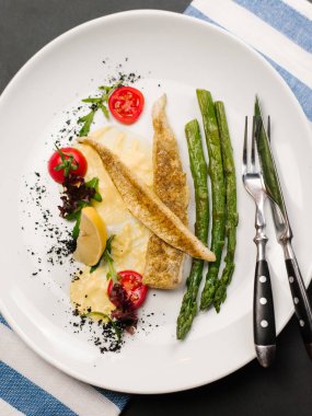 İştah açıcı Fırında Balık fileto ile kavrulmuş kuşkonmaz, cherry domates, krema sos ve limon parça beyaz tabakta servis