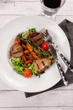 Izgara fileto mignon adet peçete, çatal ve bıçak ahşap plakalar arka plan üzerinde beyaz tabakta servis sebzeler ile Üstten Görünüm