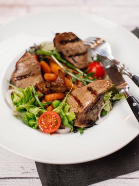 Izgara fileto mignon parçaları bebek havuç, domates, marul ve beyaz tabakta roka ile görünümünü portre