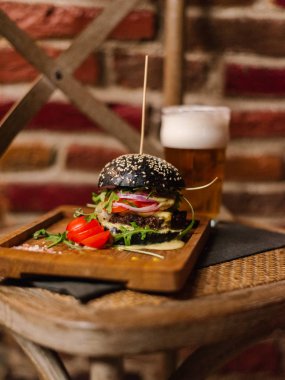 Kara Prens çizburger roka ile servis ve sandalye üzerinde soğuk bir bira ile ahşap yemek üzerine dilimlenmiş domates