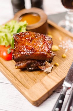Pişmiş domuz eti boyun marul, dilimlenmiş ahşap tabak üzerinde bıçak ve çatal ile domates ve baharatlı sos ile servis