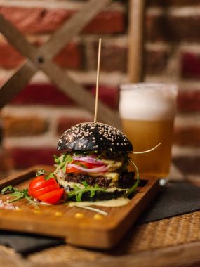 Kara Prens çizburger roka ile servis ve dilimlenmiş domates ahşap tabak ve soğuk bira