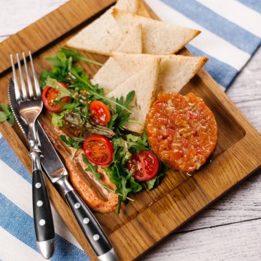 Somon tartar havyar sosu, domates, roka ve ekmek tost ve çatal bıçak takımı ile ahşap yemek servis