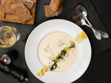 Siyah peçete, ekmek dilimleri ve siyah tablo arka plan üzerinde beyaz şarap iki kaşık ile krem çorba servis