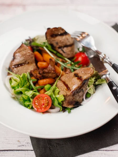 Fileto mignon parçaları ile beyaz peçete, çatal ve bıçak ile tabakta sebzeler
