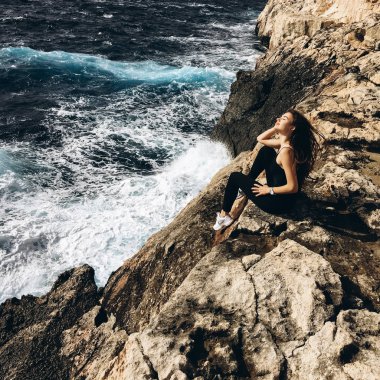 rüzgarlı gün karanlık su ile sahil, rocky Dağları üzerinde siyah giysili genç erkek görünümünü