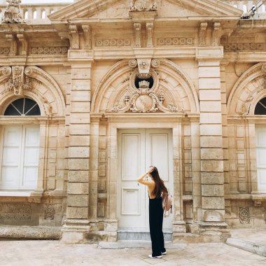 Siyah romper, sarı jumper ve dekore edilmiş vintage house yanında ayakta beyaz spor ayakkabı giyen kadın görünümünü.