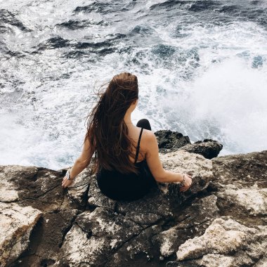 rüzgarlı gün karanlık su ile sahil, rocky Dağları üzerinde siyah giysili genç erkek görünümünü