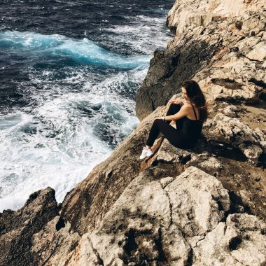 rüzgarlı gün karanlık su ile sahil, rocky Dağları üzerinde siyah giysili genç erkek görünümünü