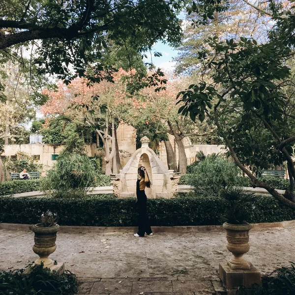 Woman wearing black romper, yellow jumper and white sneakers walking in old garden.