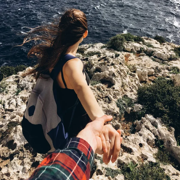 風の強い日で暗い水と海岸でロッキー山脈の上に男性の手を握ってのバックパックと若い女性の背面します — ストック写真