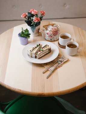 lezzetli dilim kek beyaz plaka üzerinde metin ile yakın iki beyaz fincan çay çaydanlık, çatal, peçete ve ahşap masa arka plan üzerinde çiçekler ile çekim