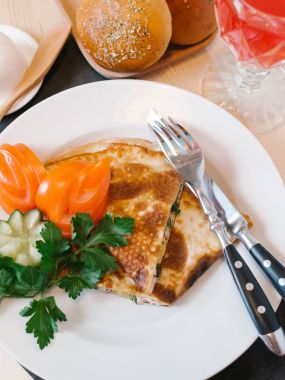 Jambon, otlar ve dilimlenmiş domates, salatalık ve maydanoz ile beyaz tabakta peynir ile doldurulmuş krep