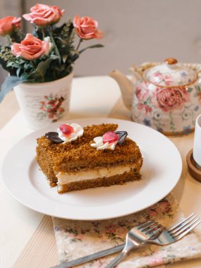 Tatlım pasta çatal, peçete, çaydanlık ve çiçekler ile beyaz tabakta servis ihale krema ile