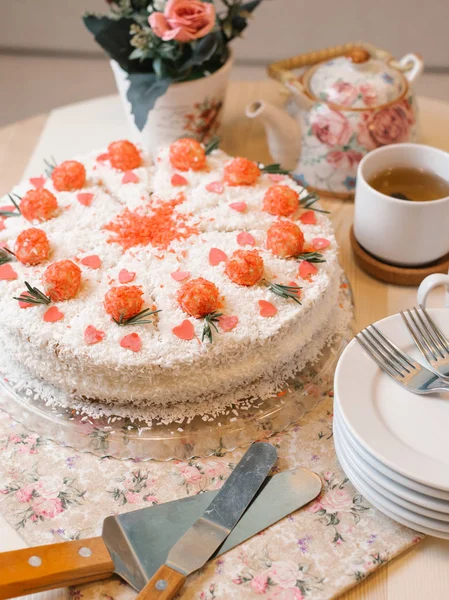 Sponge cake with tender cream, berries filling, coconut chips and decorative sweet flowers on top served with tea set, spatulas and forks