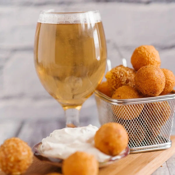 close-up of frying cheese balls with white sauce and beer on wooden board