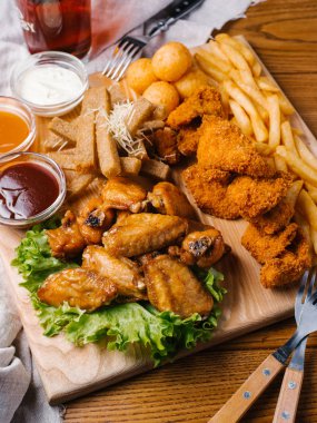 Yakın görünümü bira tabak tavuk kanat, tavuk nuggets, sarımsak tost ve farklı sos ile patates kızartması, marul hizmet koyu bira cam ve çatal ile ahşap kesme tahtası üzerinde
