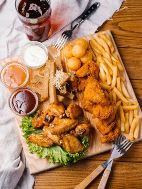 Yakın görünümü bira tabak tavuk kanat, tavuk nuggets, sarımsak tost ve farklı sos ile patates kızartması, marul hizmet koyu bira cam ve çatal ile ahşap kesme tahtası üzerinde