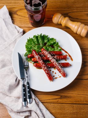 Wite tabakta susam ve marul sosis ızgara Avcılık Bıçak, çatal, karanlık bira cam ve karabiber değirmeni ahşap tablo