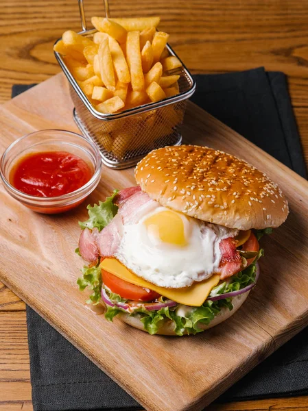 Çizburger pastırma ve omlet, ahşap kesme tahtası ve gri peçete üzerinde hizmet sepeti ve tatlı ketçap patates kızartması ile