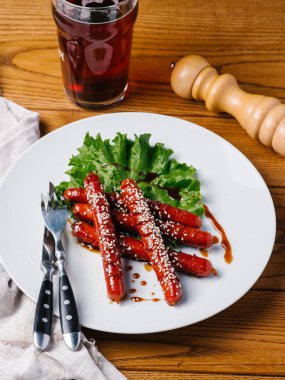 Wite tabakta susam ve marul sosis ızgara Avcılık Bıçak, çatal, karanlık bira cam ve karabiber değirmeni ahşap tablo