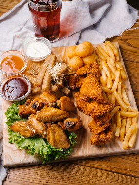 Bira plaka tavuk kanatları, tavuk nuggets, sarımsak tost ve farklı sos ile patates kızartması, marul hizmet ahşap kesme tahtası koyu bira cam üzerinde