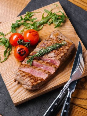 Orta nadir sığır biftek ızgara domates ile taze pişmiş, biberiye ve roka ile bıçak ve çatal ahşap kesme tahtası ve gri peçete servis