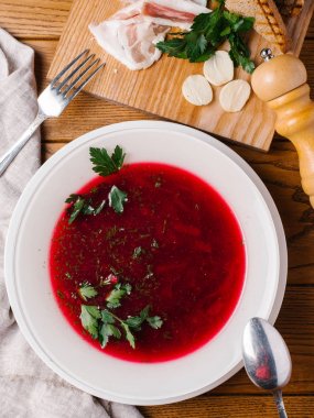 Maydanoz, kaşık, çatal, pastırma, ekmek tost, karabiber öğütücüsü ve ekşi krema ahşap masanın üzerine dilimlenmiş beyaz kase geleneksel pancar çorbası servis