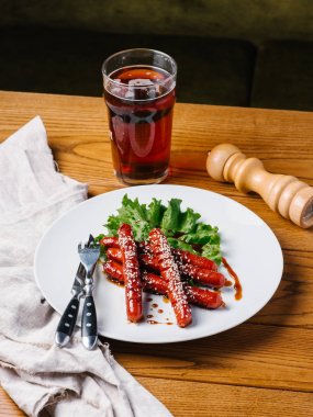 Wite tabakta susam ve marul sosis ızgara Avcılık Bıçak, çatal, karanlık bira cam ve karabiber değirmeni ahşap tablo