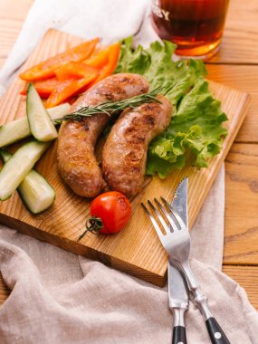 Izgara sosis taze dilimlenmiş biber, cucumers, domates, marul ahşap kesme tahtası ve karanlık bira cam ile servis Görünümü Kapat