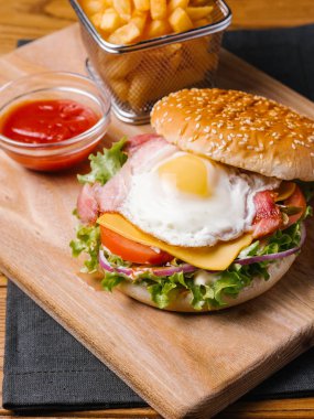 Çizburger pastırma ve omlet, ahşap kesme tahtası ve gri peçete üzerinde hizmet sepeti ve tatlı ketçap patates kızartması ile
