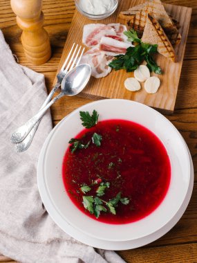 Geleneksel pancar çorbası görünümünü closeup maydanoz, kaşık, çatal, pastırma, ekmek tost, karabiber öğütücüsü ve ekşi krema ahşap masanın üzerine dilimlenmiş beyaz kase hizmet