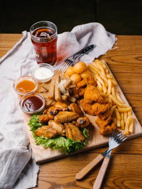 Bira plaka tavuk kanatları, tavuk nuggets, sarımsak tost ve farklı sos ile patates kızartması, marul hizmet koyu bira cam ve çatal ile ahşap kesme tahtası üzerinde