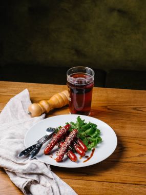 İştah açıcı ızgara avcılık sosis susam ve marul wite tabakta bıçak, çatal, karanlık bira cam ve karabiber değirmeni ahşap tablo