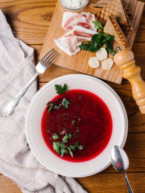 Maydanoz, kaşık, çatal, pastırma, ekmek tost, karabiber öğütücüsü ve ekşi krema ahşap masanın üzerine dilimlenmiş beyaz kase geleneksel pancar çorbası servis