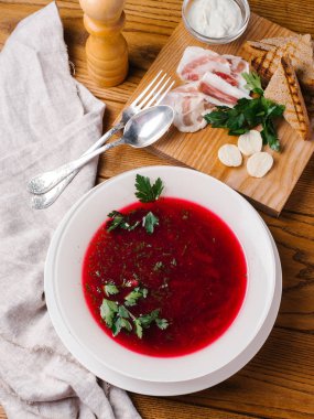Geleneksel pancar çorbası görünümünü closeup maydanoz, kaşık, çatal, pastırma, ekmek tost, karabiber öğütücüsü ve ekşi krema ahşap masanın üzerine dilimlenmiş beyaz kase hizmet