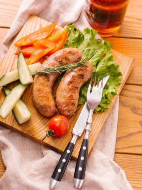 Taze dilimlenmiş biber, cucumers, domates, marul ahşap kesme tahtası ve karanlık bira cam ile ızgara sosis servis