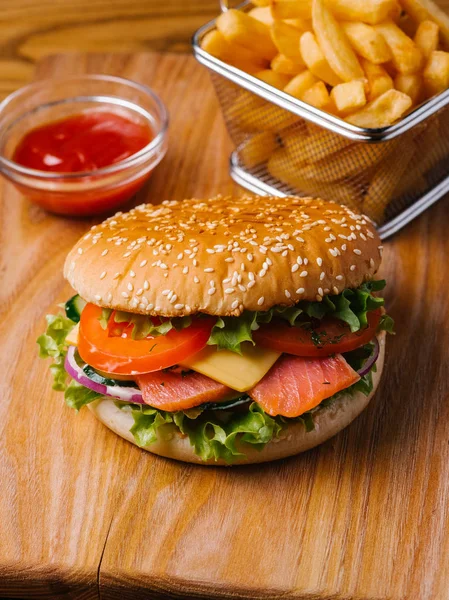 Leziz yemek sepeti ve tatlı ketçap ahşap kesme tahtası ve gri peçete üzerinde hizmet veren kızarmış patates somon çizburger, dahil olmak üzere