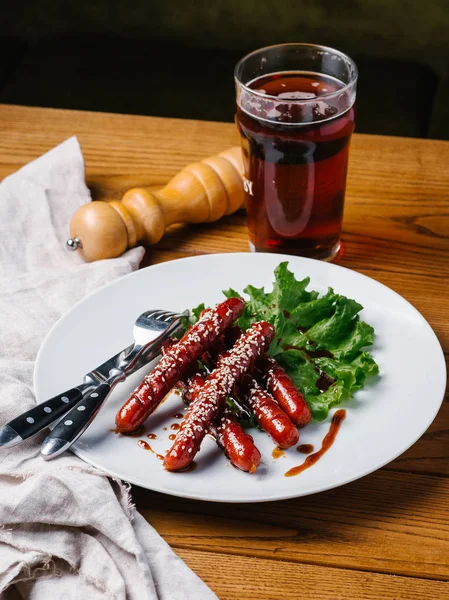 Wite tabakta ızgara avcılık sosis susam ve marul Görünümü Kapat bıçak, çatal, karanlık bira cam ve karabiber değirmeni ahşap tablo