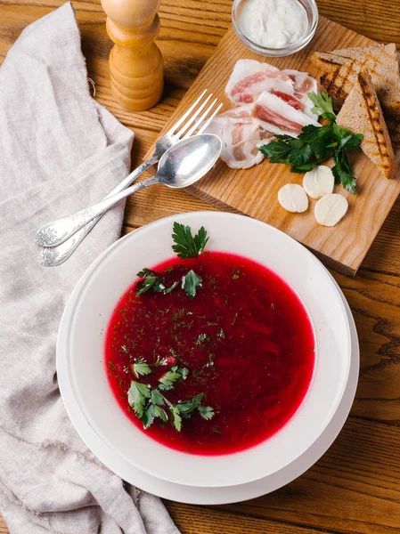 Geleneksel pancar çorbası görünümünü closeup maydanoz, kaşık, çatal, pastırma, ekmek tost, karabiber öğütücüsü ve ekşi krema ahşap masanın üzerine dilimlenmiş beyaz kase hizmet