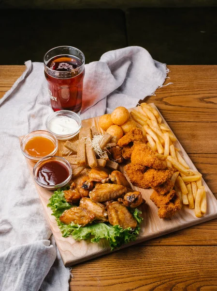 Bira plaka tavuk kanatları, tavuk nuggets, sarımsak tost ve farklı sos ile patates kızartması, marul hizmet ahşap kesme tahtası koyu bira cam üzerinde