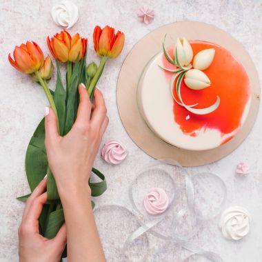 Erkek bileşimi holding lale, beyaz eller ve dekore edilmiş kırmızı pasta, şerit ve meringues