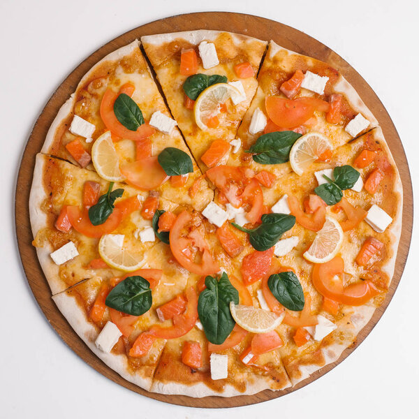 Top view of pizza with salmon, feta, basil leaves, tomatoes, lemon slices and mozzarella served on pizza plate