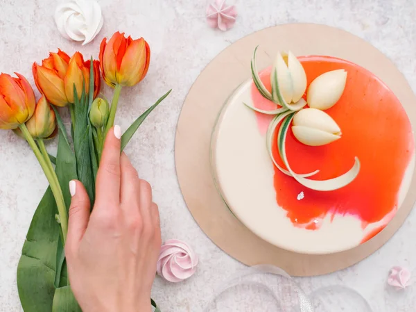 女性手捧红色郁金香 白色和红色装饰蛋糕 蛋白甜饼和丝带的食物构成 — 图库照片