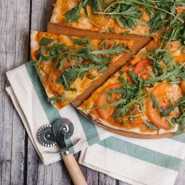 Pizza kesici ve çizgili peçete ile ahşap pizza tabakta closeup Pizza domates sosu, pesto sos, mozzarella peyniri, roka ve domates ile servis