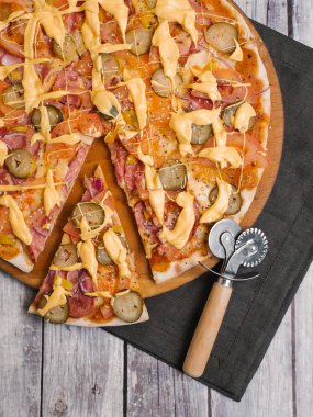 Pizza domates sosu, peynir sos, mozzarella peyniri, domates, sosis, turşu, tatlı soğan, closeup sarı biber pizza kesici ve ahşap plakalar arka plan üzerinde koyu peçete ile ahşap pizza tabakta