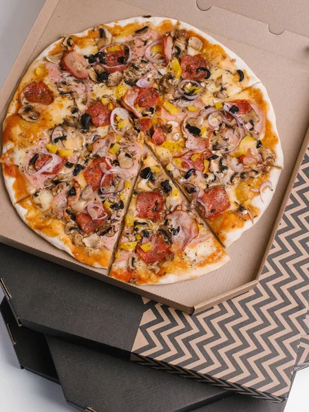 Pizza with tomato sauce, mozzarella, ham, sausages, olives, sweet onions, yellow peppers and mushrooms served in cardboard box