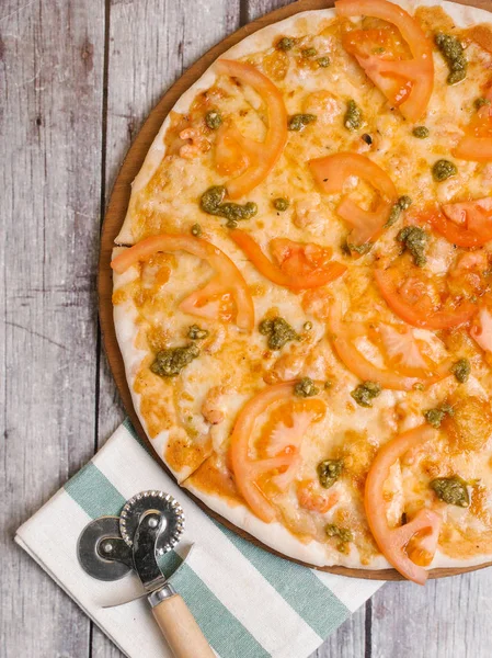 Pizza with tomato sauce, pesto sauce, mozzarella and tomatoes served on wooden pizza plate with pizza cutter and striped napkin